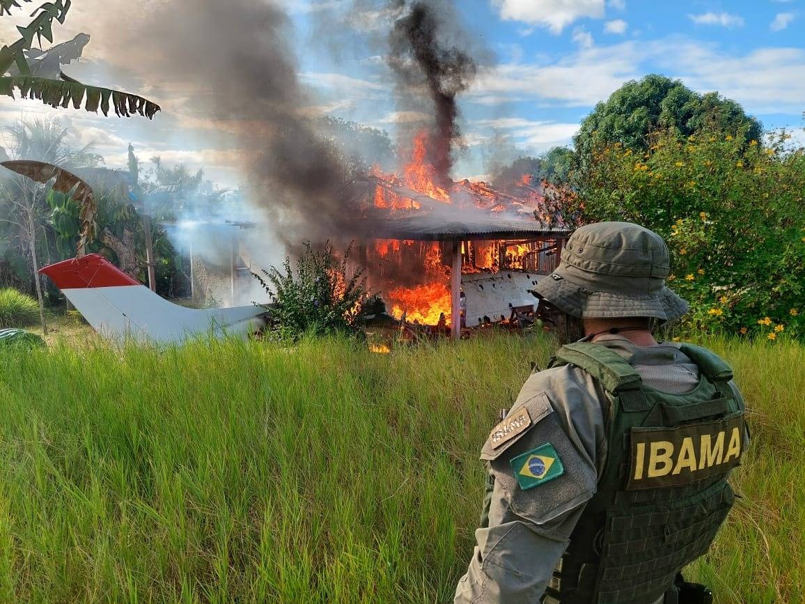 Agente do Ibama durante operação de combate ao garimpo no dia 07/02/2023 na terra indígena Yanomami. Na imagem é possível ver o agente de costas para a câmera com o uniforme do Ibama. À sua frente há uma aeronave pegando fogo em meio a um campo aberto na floresta