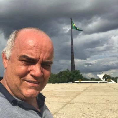 Wilmar Cesário Rosa, um homem branco de cabelos grisalhos e calvo aparece na imagem em frente a uma bandeira do brasil hasteada em um mastro, ele usa uma camisa azul de gola e botões.