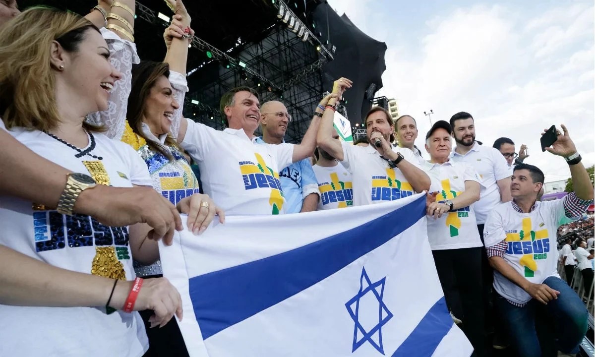 O ex-presidente Jair Bolsonaro aparece ao lado de fiéis e pastores no palco da Marcha para Jesus 2019. Eles seguram a bandeira de Israel