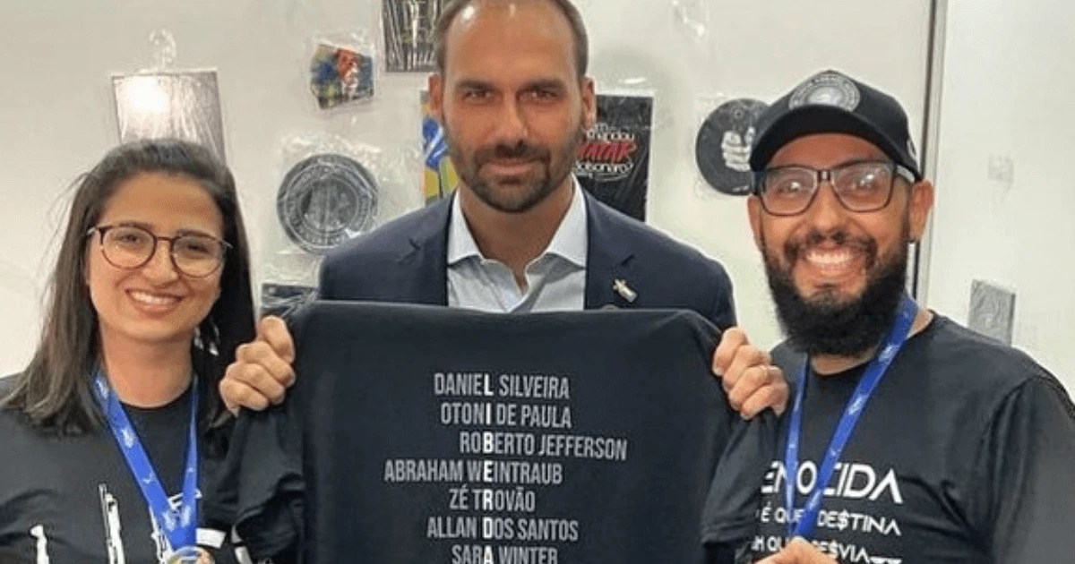 Eduardo Bolsonaro (meio), posa para a foto segurando uma camiseta da loja ''Camisetas Opressoras, ao seu lado Denise Bueno (à esq) e Wilker Delkerson Amaral (à dir)