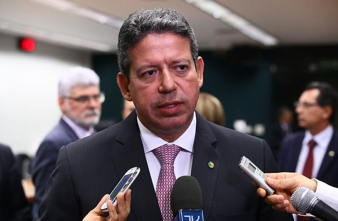 Presidente da Câmara dos Deputados, Arthur Lira. Ele é um homem branco de cabelos grisalhos e olhos castanhos. Lira veste terno cinza com camisa social branca e gravata colorida