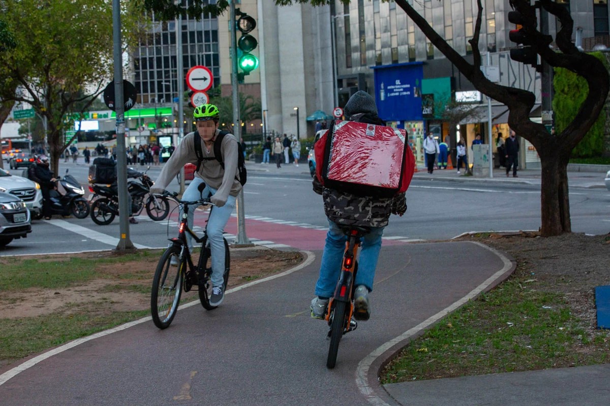 Na imagem entregadores de empresas de aplicativo andam em suas bicicletas a caminho de seus destinos.