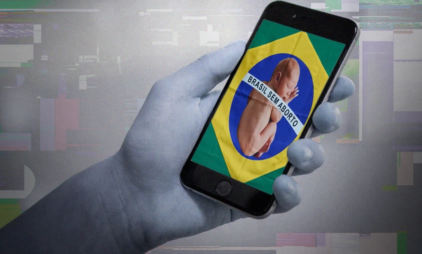 Ilustração mostra mão segurando um celular com uma imagem de um bebê deitado sobre a bandeira do Brasil com a frase "Brasil sem aborto"