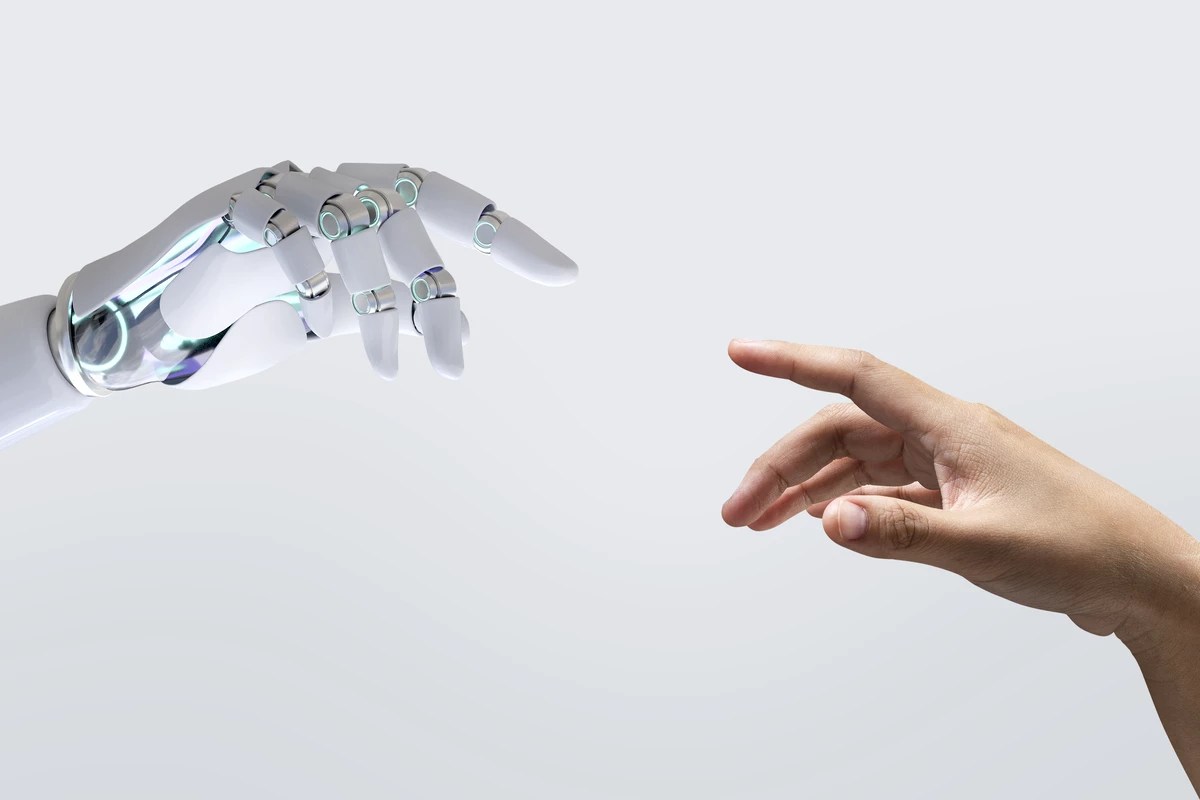Mão robótica simbolizando o uso de inteligência artificial suspensa no ar tentando tocar uma mão humana