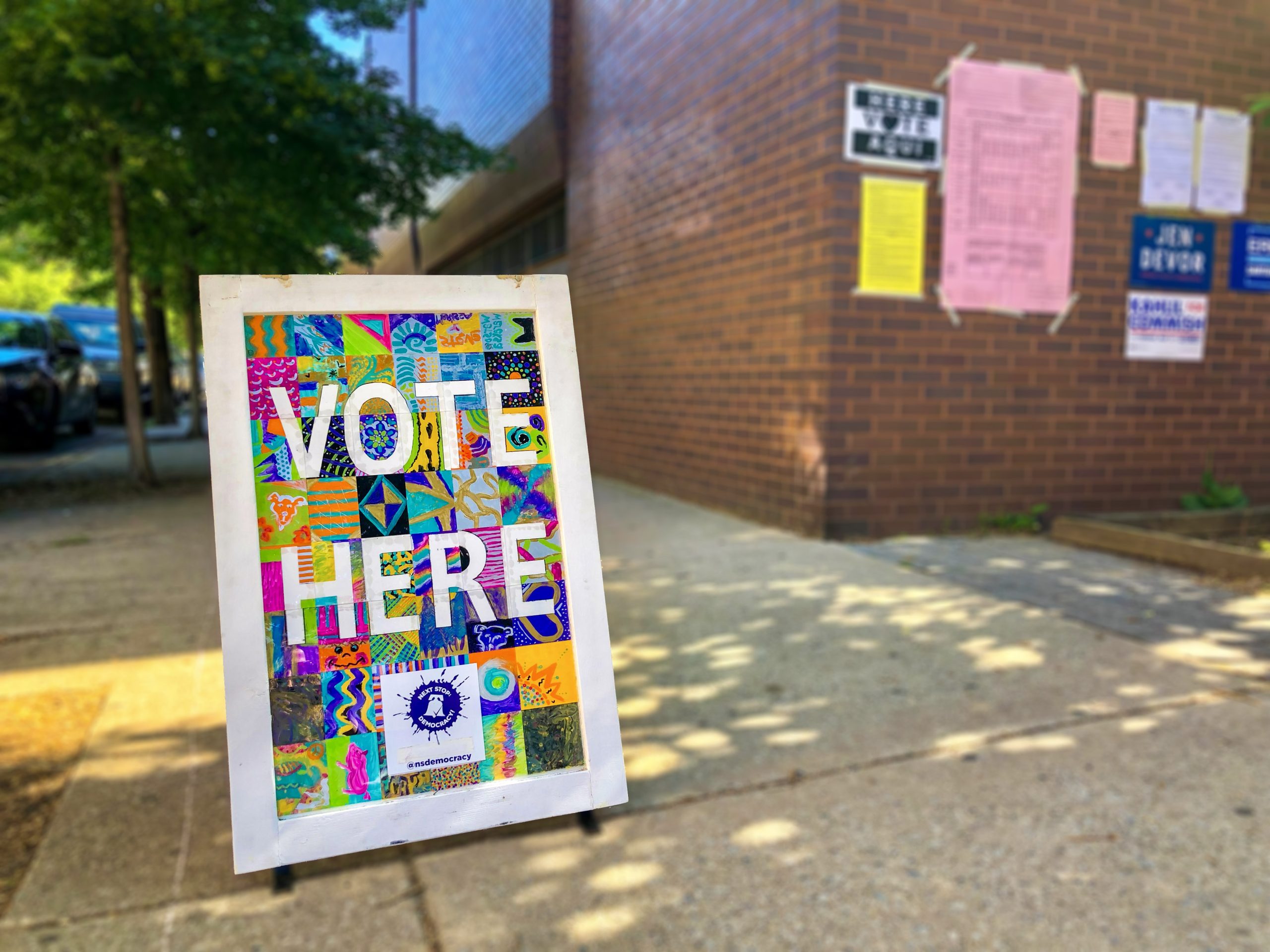 Sidewalk chalk sign with colorful message declaring VOTE HERE.