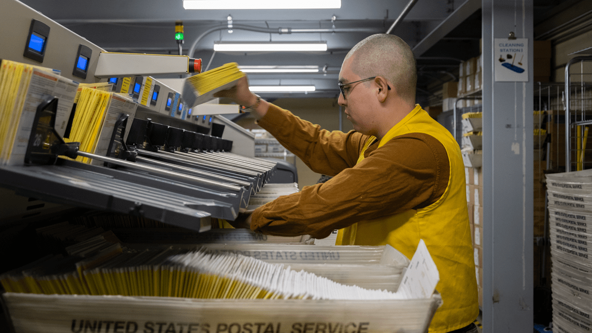 Staff members at the San Bernardino Registrar of Voters organize sealed ballot envelopes into a high speed electronic sorting machine that will capture the barcodes and signatures.