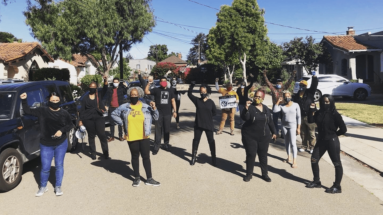 Oakland Councilmember Carroll Fife stands in the center, as she joins community members in holding their fists up.