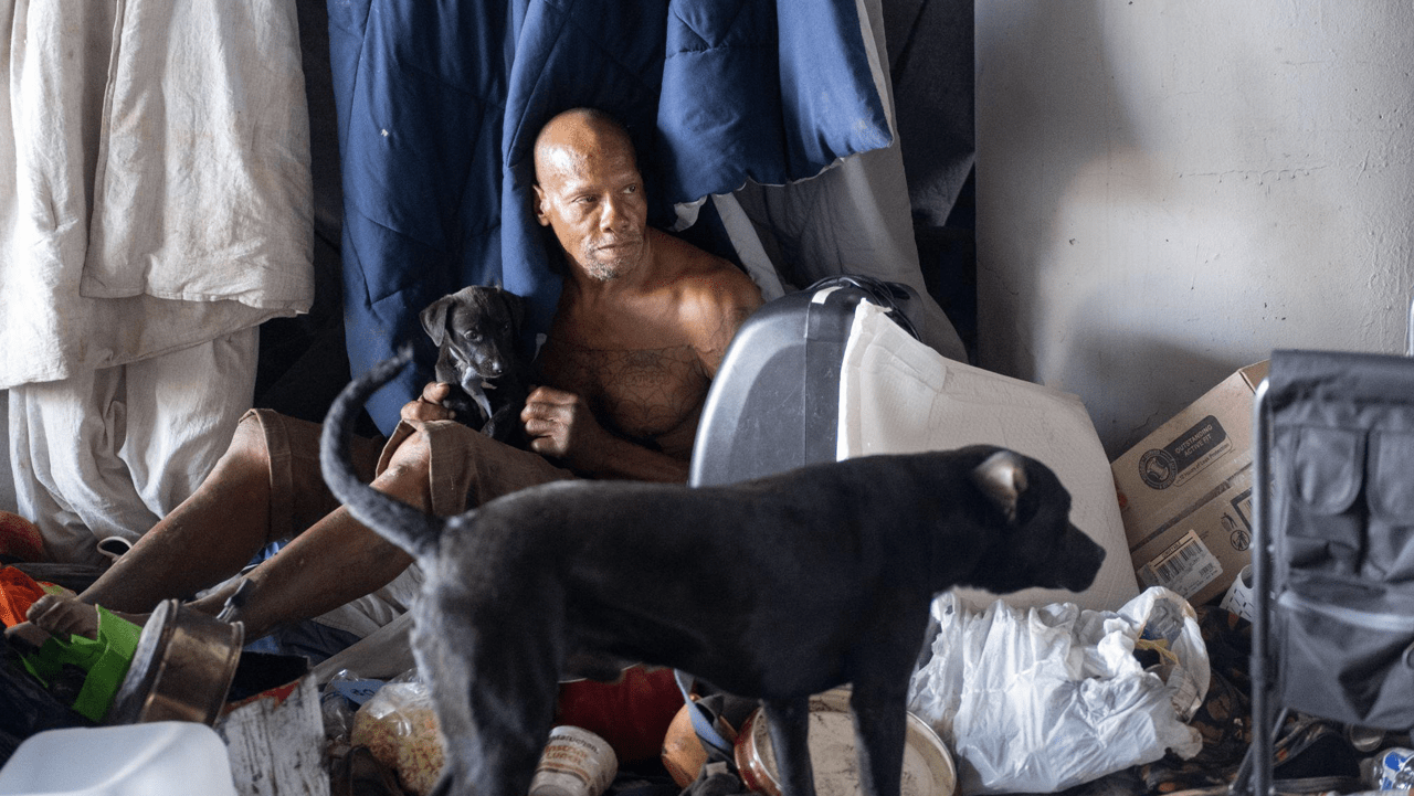 Redbone sits in his tent while holding one of his puppies in his encampment in Riverside on July 11, 2024. He has lived on the streets for the past 13 years and says the heat increases every year, forcing him to adapt. As heat waves swathe Southern California, the Inland Empire’s homeless population faces increasing health risks.