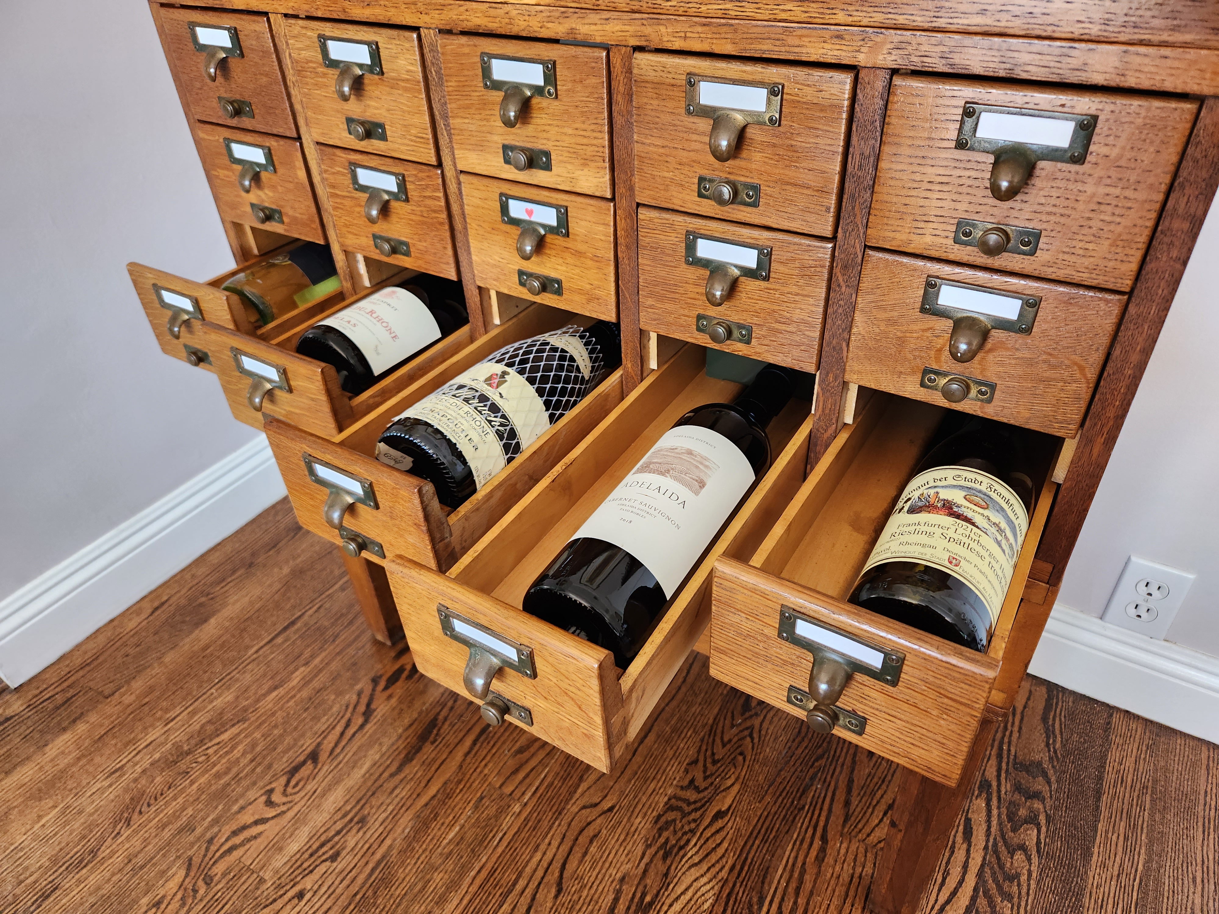 Angle on a row of five library card catalog drawers open with bottles of wine displayed in each.