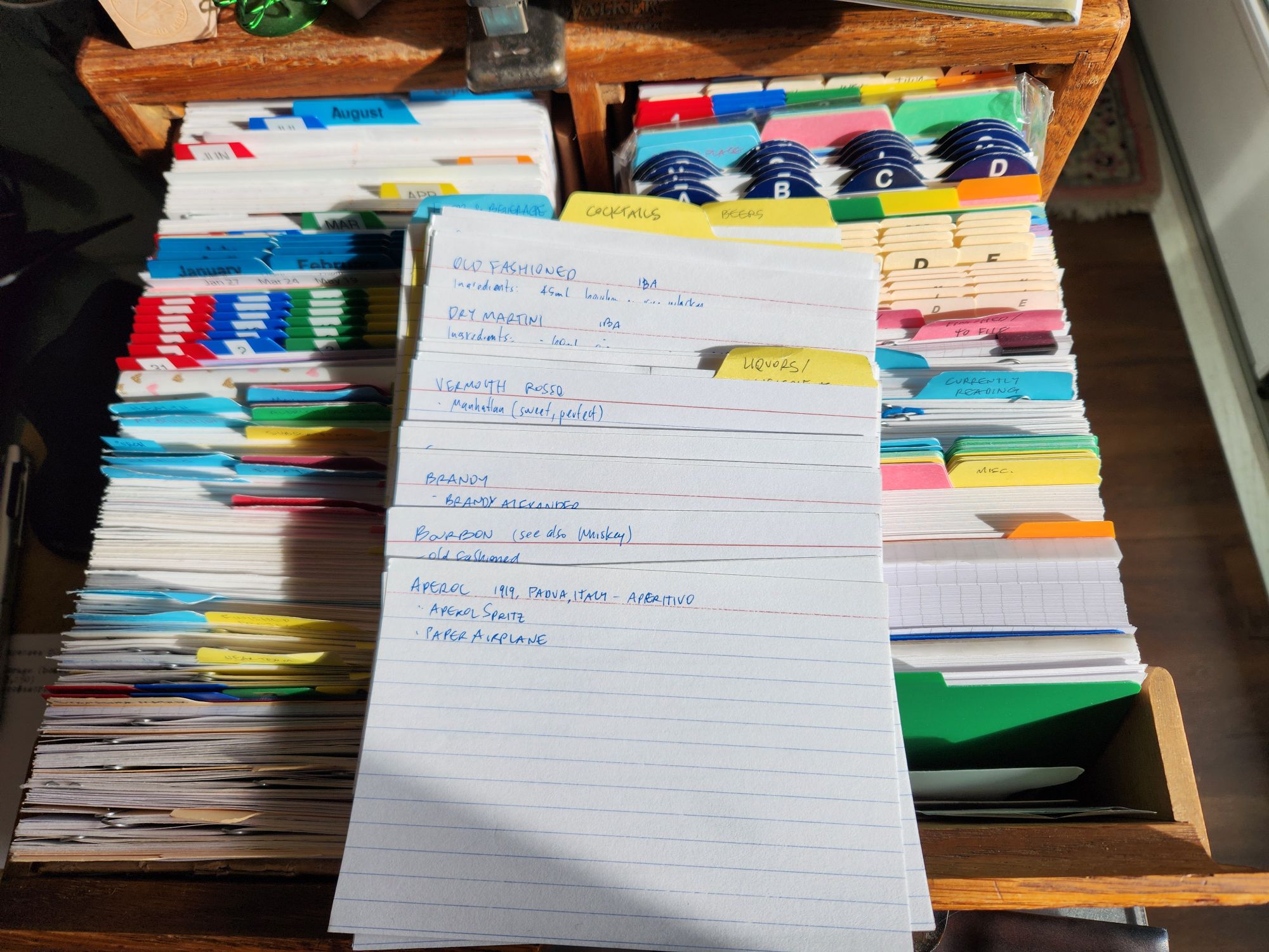 Column of index cards displaying tabs for cocktails and cocktail ingredients and sample cards showing for various ingredients (aperol, bourbon, brandy, vermouth) and related drinks one could make with them (dry martini, old fashioned).