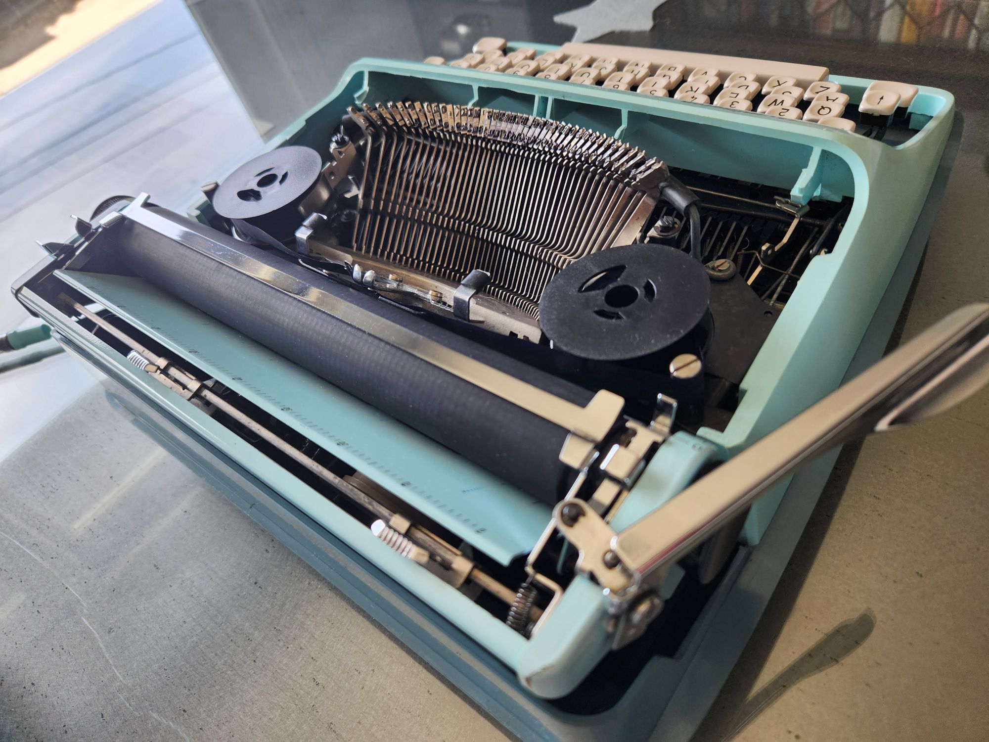 Angled view from the right hand side and behind of the Remington Streamliner typewriter with the hood removed to provide a view of the typebasket, typebars, ribbon spools and the platen.