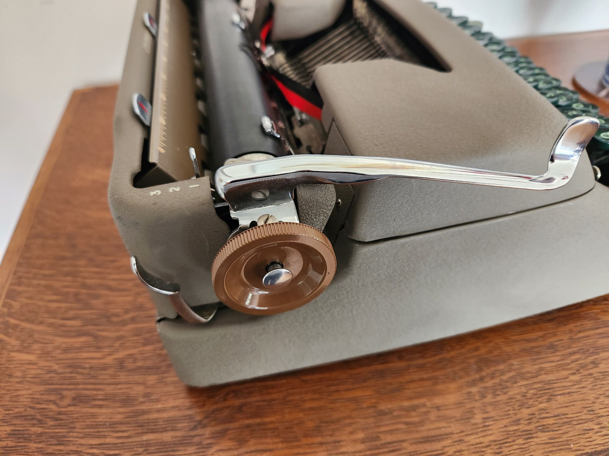 view of the left side of the typewriter which includes a dark brown plastic platen knob with a silver button on it