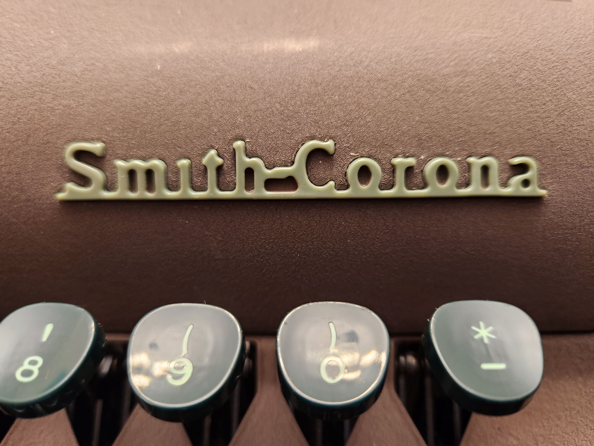 Close up of the light green plastic Smith-Corona badge on the hood of the typewriter.