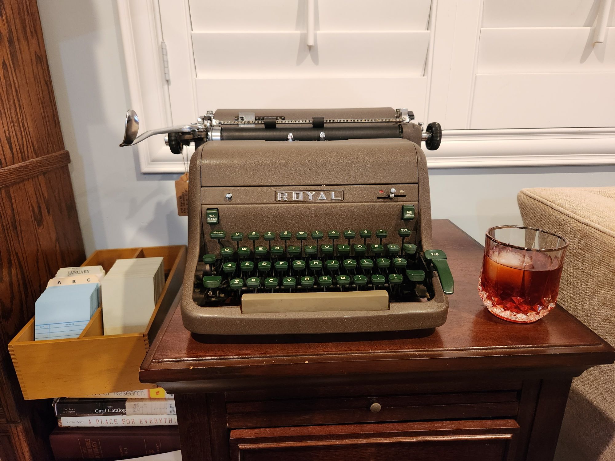 A large standard Royal HH typewriter on a side table next to an old fashioned glass with a Negroni in it. 