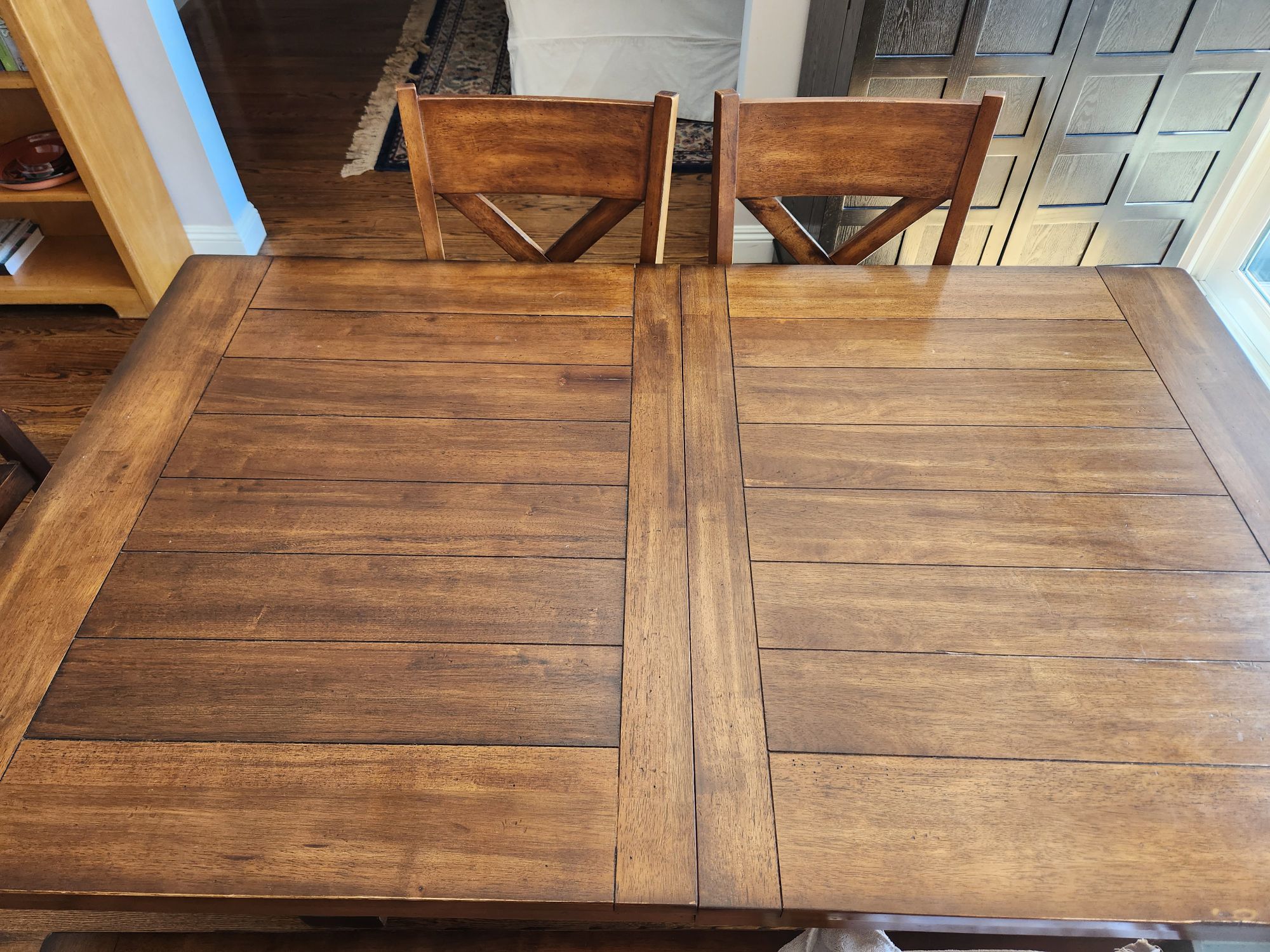 An empty wooden table with some wooden chairs on the far side.