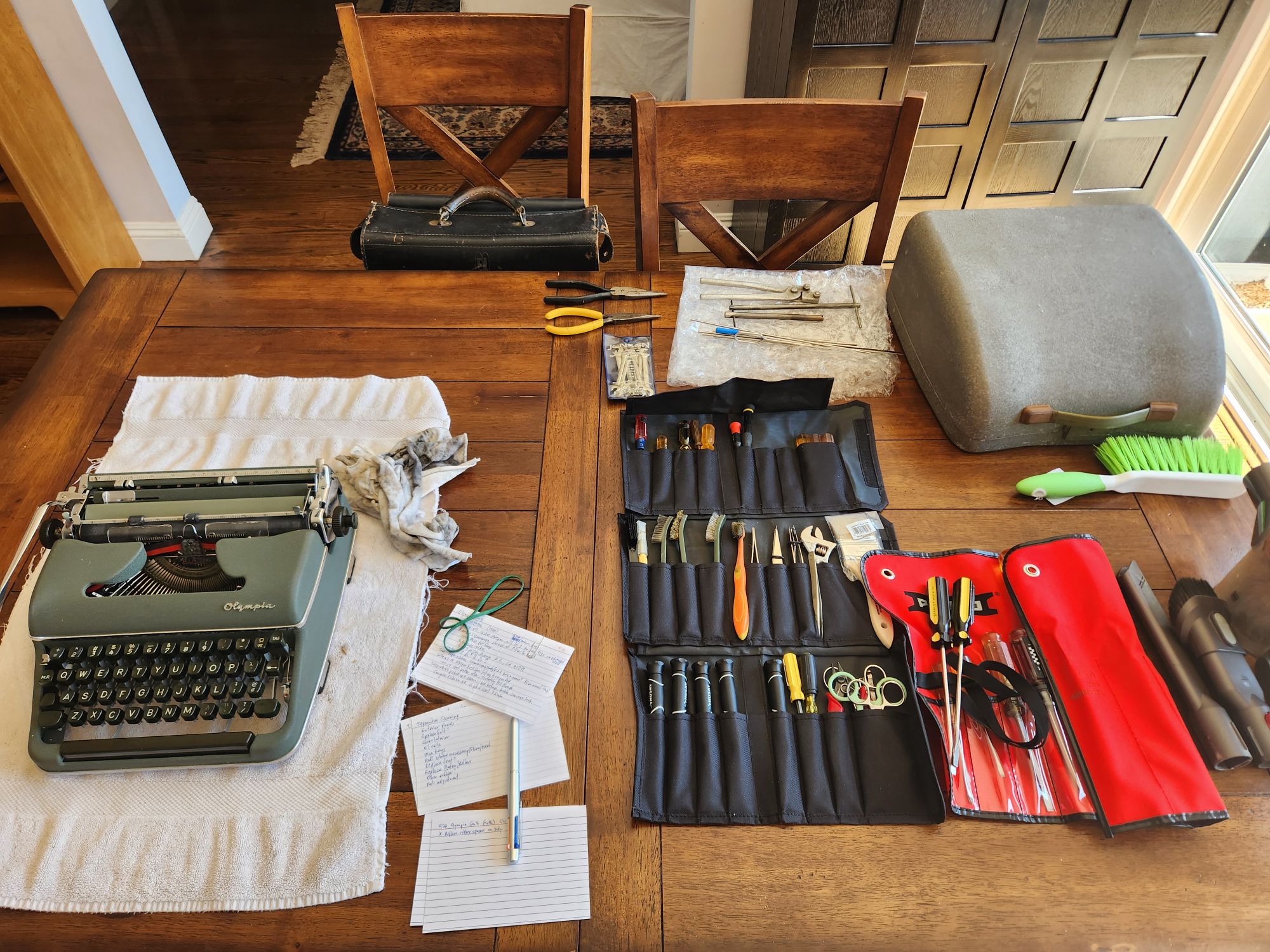 The leather toolcase has been emptied and now sits in the chair opposite the typewriter. Several tool pouches full of tools have appeared between the typewriter and the case.