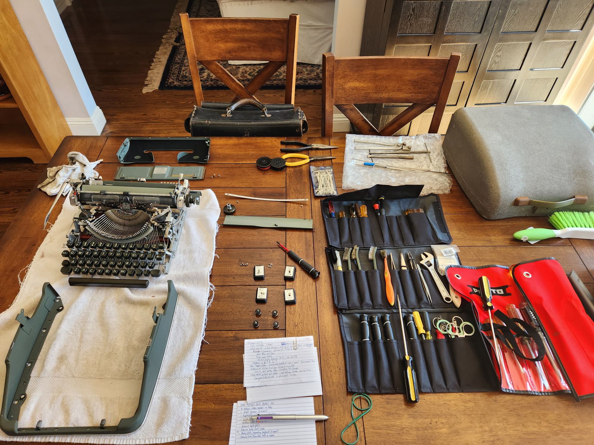 The typewriter hood and several pieces have been disassembled and appear on the table around the towel and the body of the typewriter.