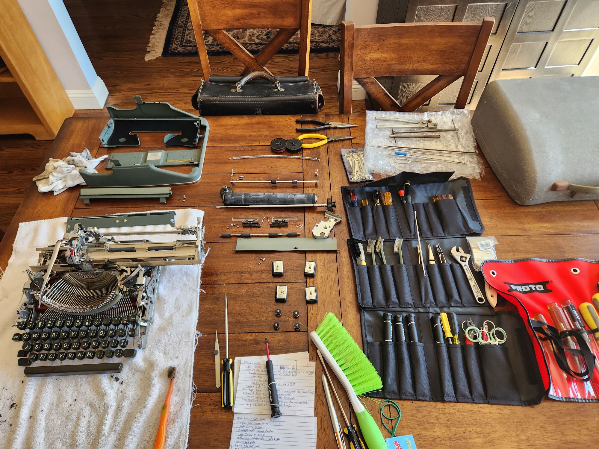 The platen and even more pieces have been removed from the typewriter and its carriage. They sit above and to the side of the typewriter and the layout of tools.