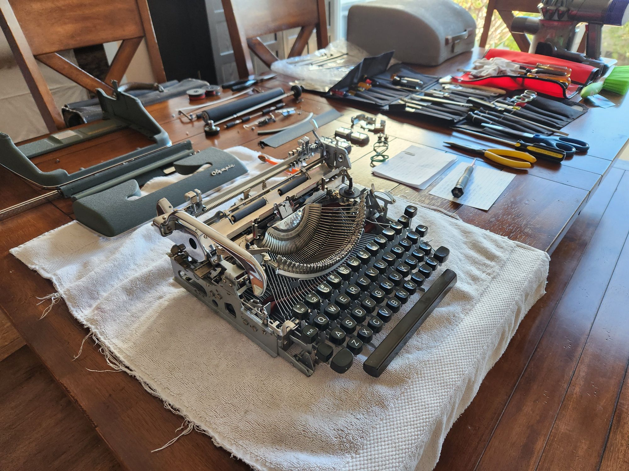 Finally, we see a different angle of the typewriter looking across the table. In the front is the naked typewriter on the hand towel which is surrounded by it's now cleaned body panels, platen, feet, and various other parts, screws, and springs. In the background we see the tools including many screwdrivers in their tool bags.