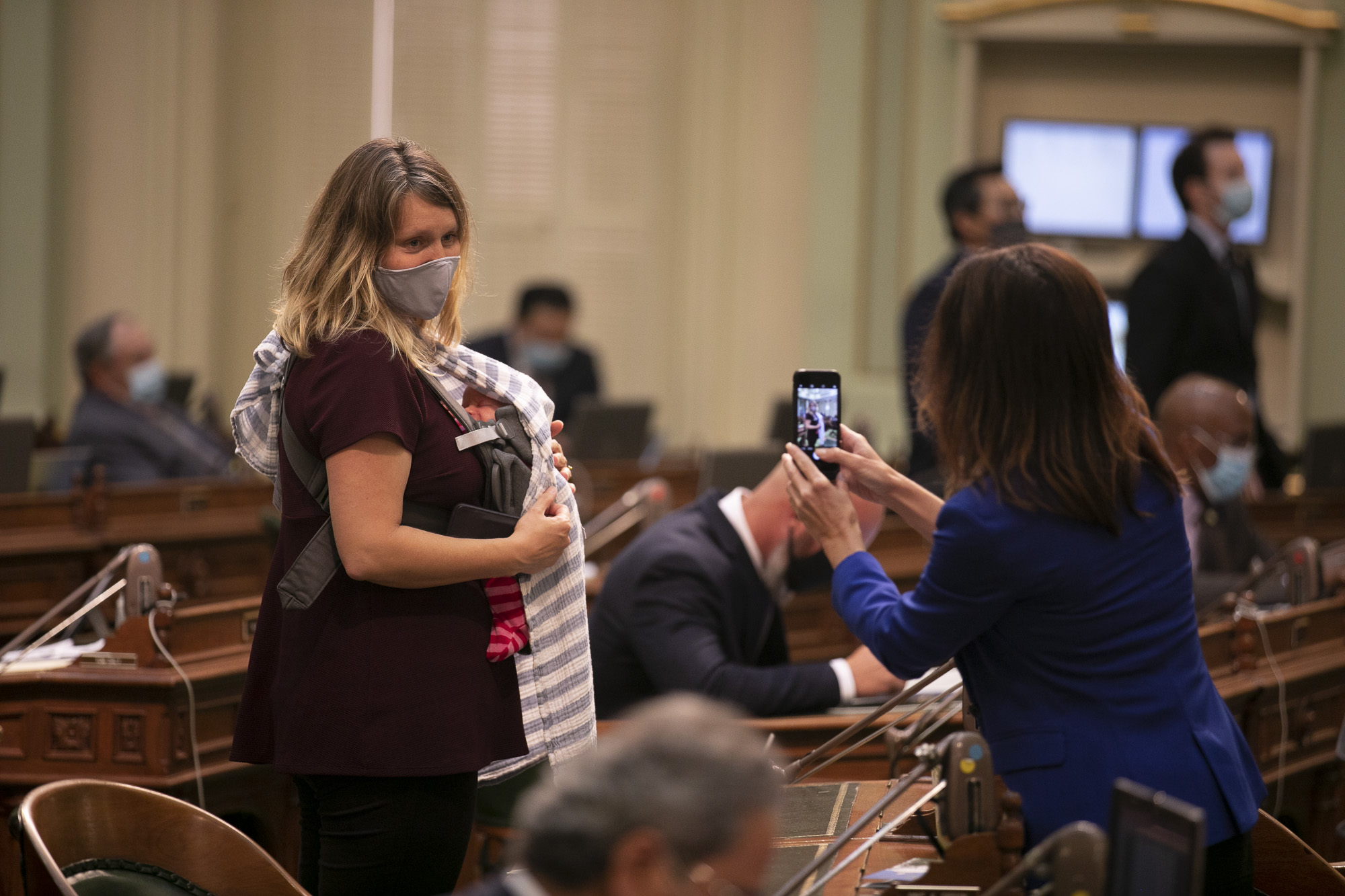 Assemblymember Buffy Wicks poses with her newborn baby on the assembly floor as Assemblymember Cottie Petrie-Norris snaps a photo with her phone on Aug. 31, 2020. Photo by Anne Wernikoff for CalMatters