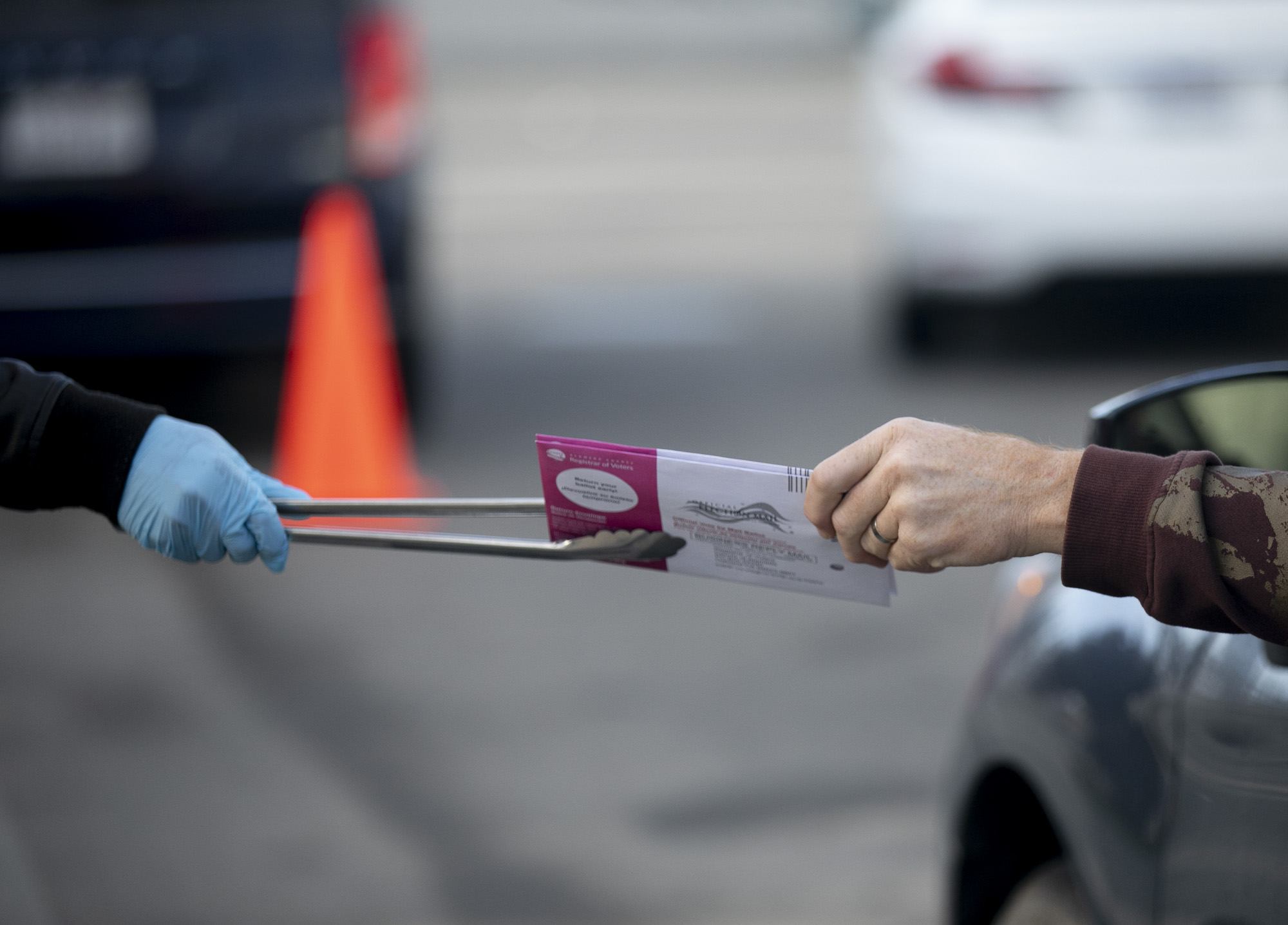 Poll workers use tongs to collect ballots and hand out stickers at a curbside voting location at Alameda County courthouse on Nov. 3, 2020. Photo by Anne Wernikoff for CalMatters