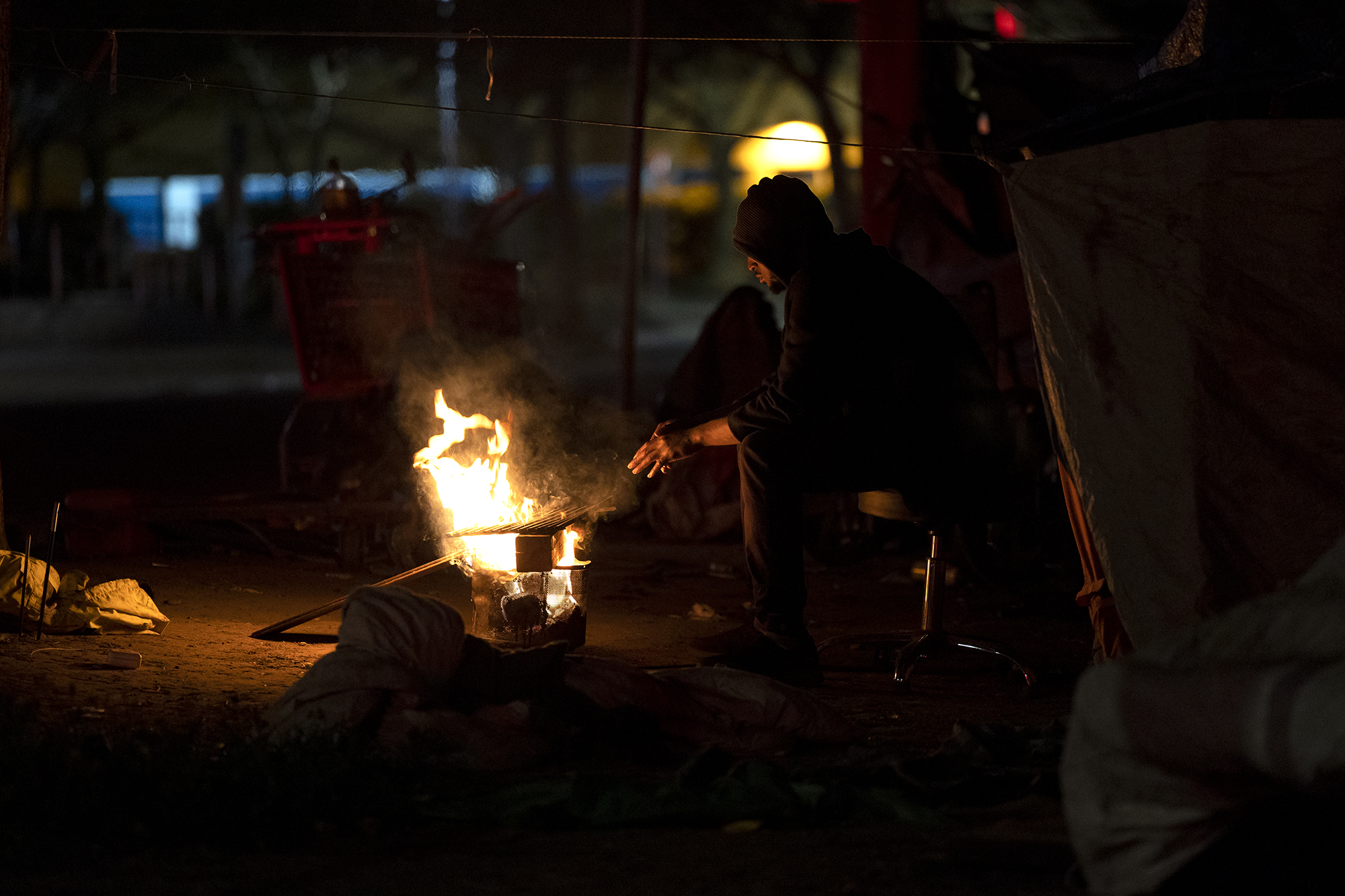 Muhammad, who declined to provide his last name, warms his hands at a fire next to his tent in Sacramento. Feb. 24, 2022. Photo by Miguel Gutierrez Jr., CalMatters
