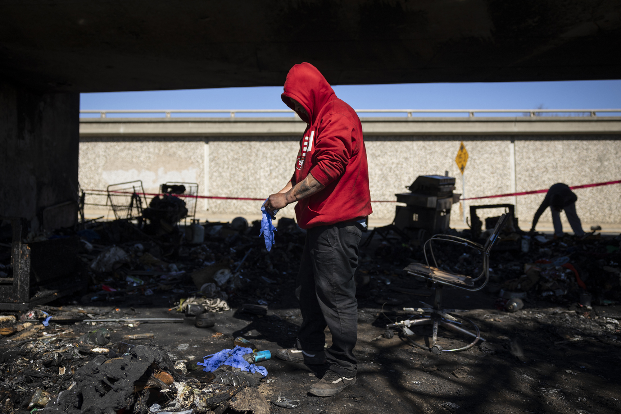 John Vasquez, 61, sorts through the remains of a fire at a homeless encampment under Highway 80, near 14th Street, in Sacramento on Feb. 24, 2022. Photo by Miguel Gutierrez Jr., CalMatters