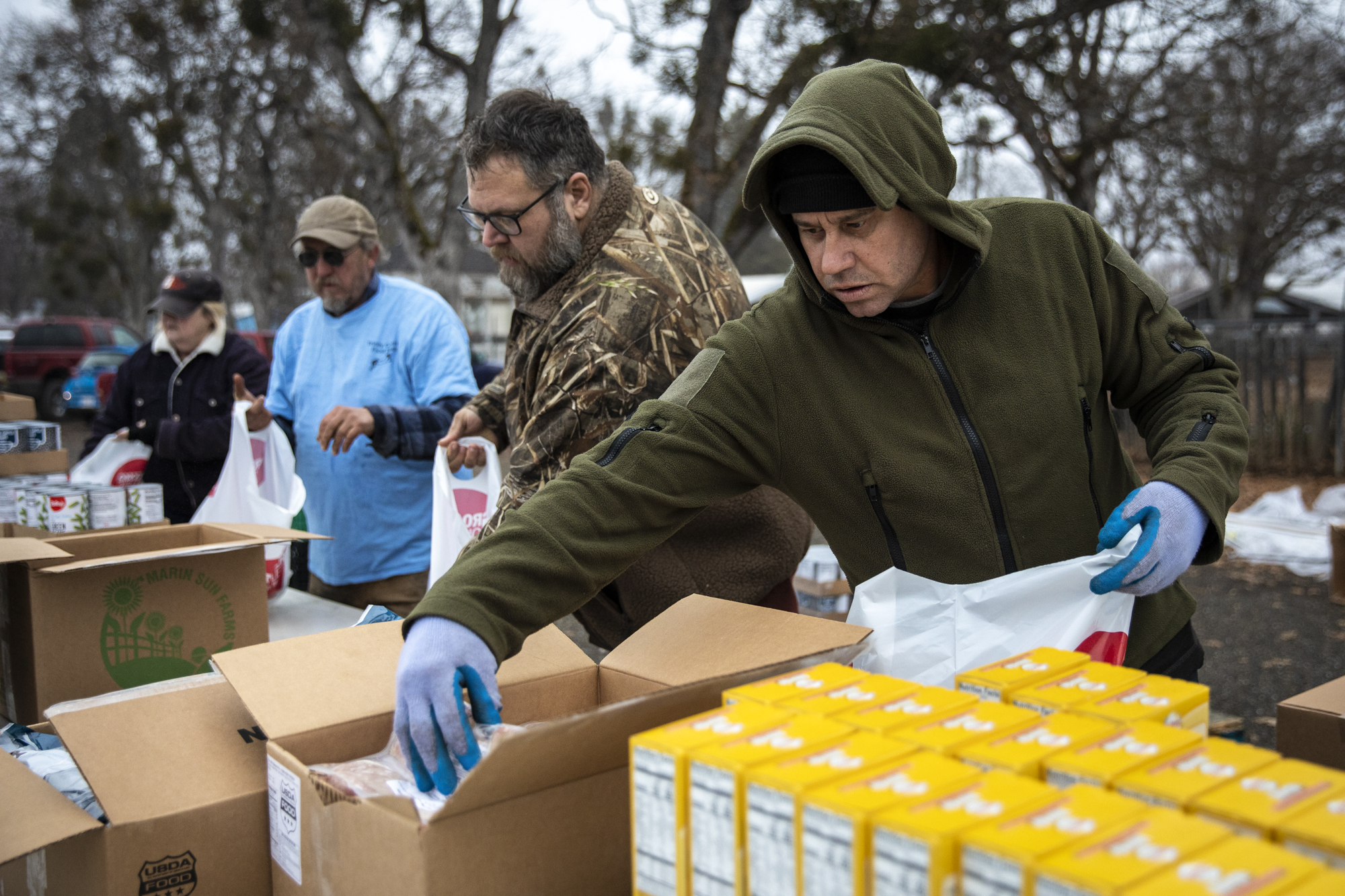 Volunteers Jeff Mummy (right), Michael Merrill (center) and others prepare bags of food for distribution by the Trinity County Food Bank at the Trinity County Fairgrounds on Feb. 8, 2023. 