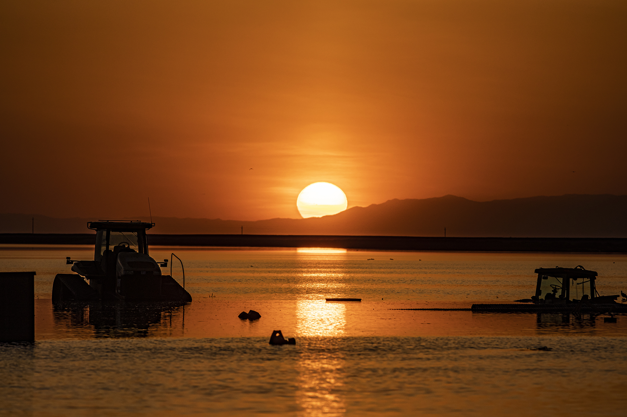 Sunset above the floodwaters in farmland with submerged tractors and farming equipment in Hansen Ranches south of Corcoran on April 26, 2023.