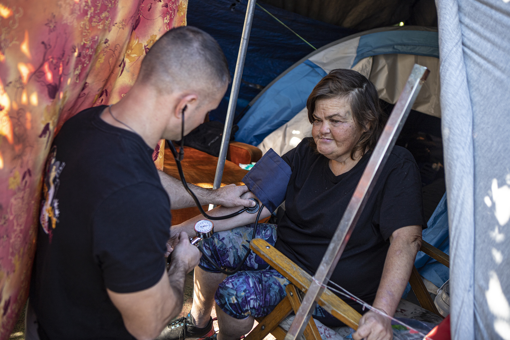 Physician's assistant Brett Feldman checks Carla Bolen's blood pressure while in her encampment at the Figueroa Street Viaduct above Highway 110 in Elysian Valley Park in Los Angeles on Nov. 18, 2022.