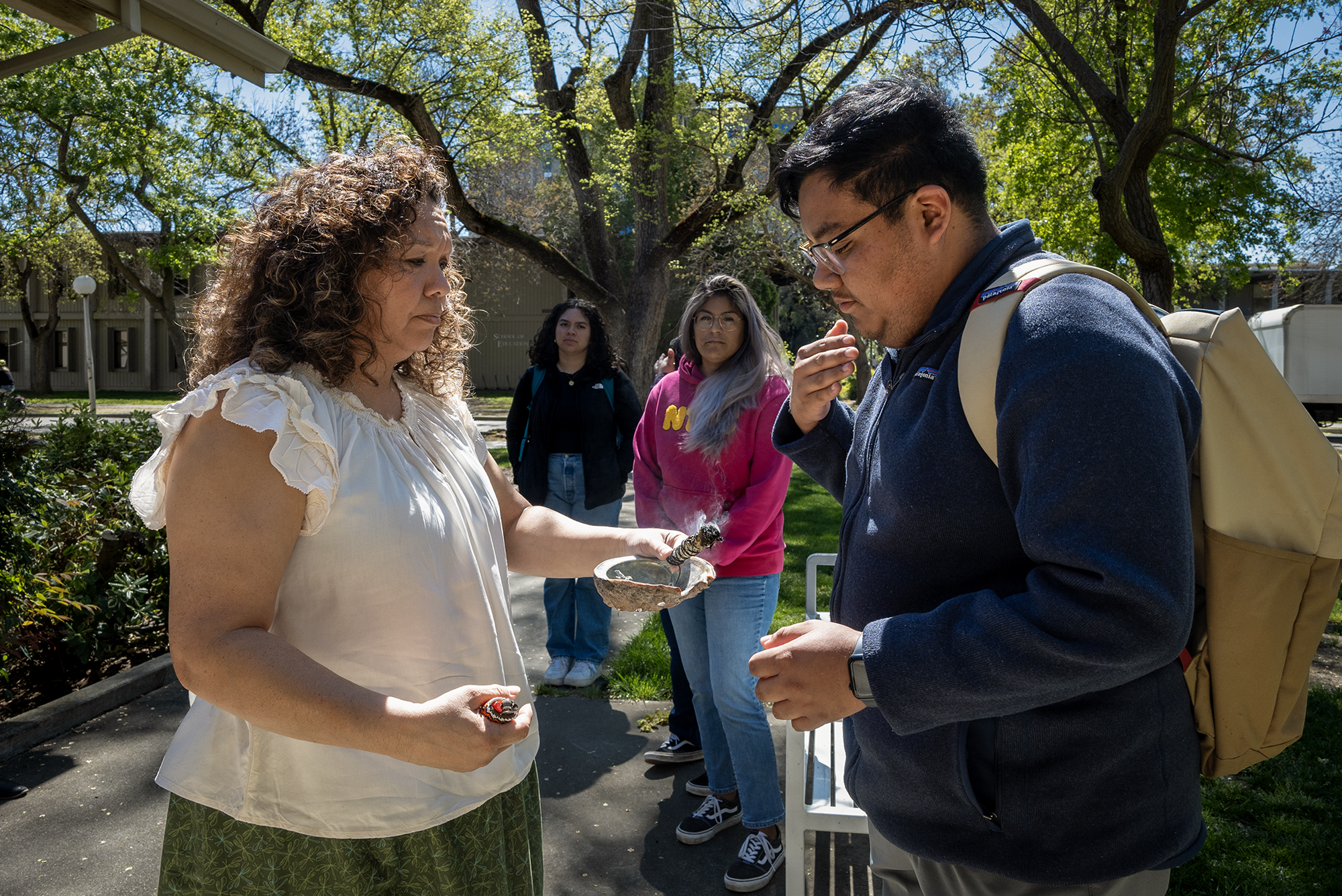 Carlos Morales and Michelle Villegas-Frazier participate in a sage burning ritual outside of the Native American Academic Student Success Center at UC Davis on April 1, 2024. Photo by José Luis Villegas for CalMatters