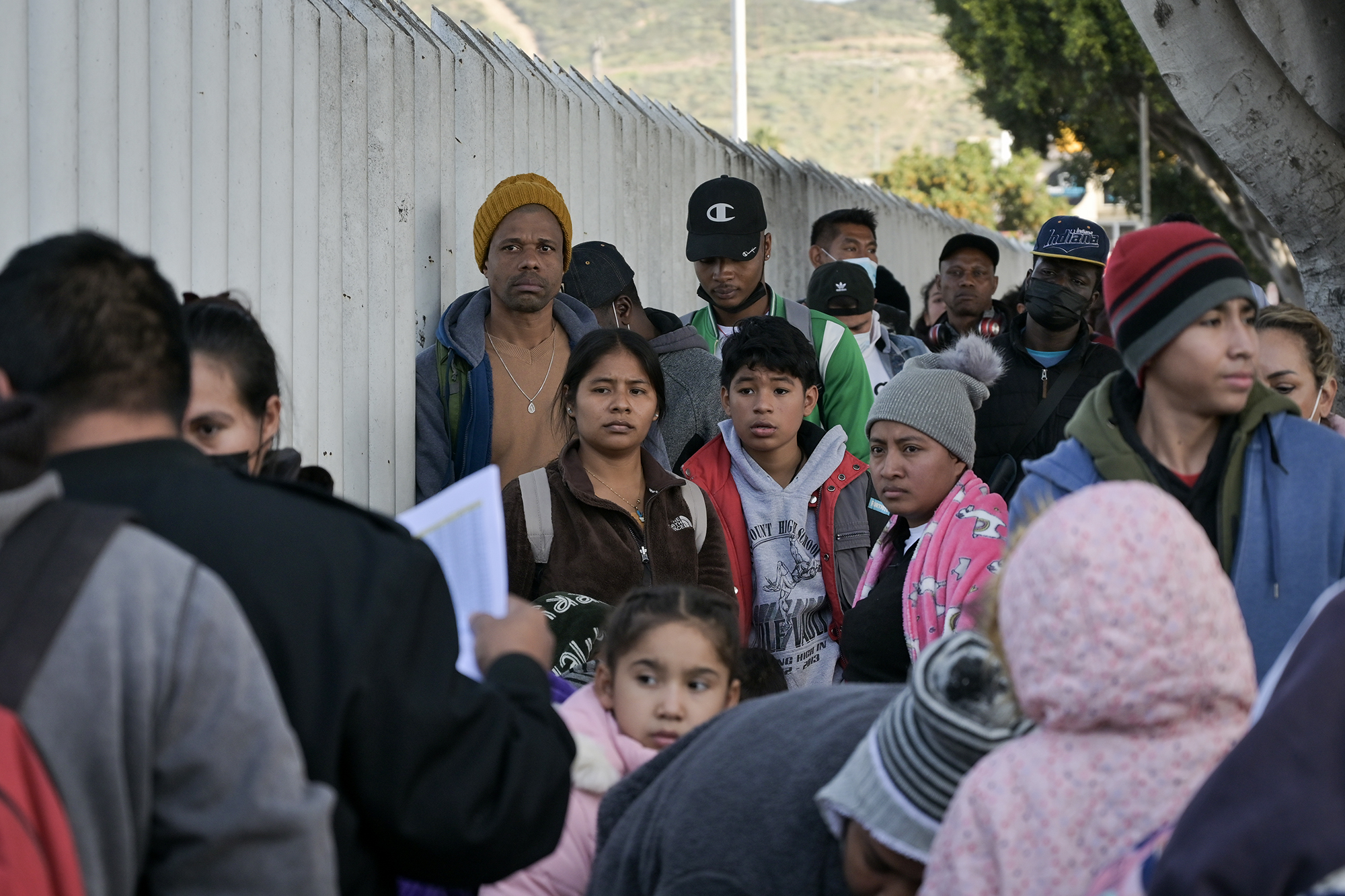 Migrants form a line to enter the U.S. and seek asylum through El Chaparral port of entry in San Diego at the Mexico border on Dec. 22, 2022. Photo by Carlos A. Moreno for CalMatters