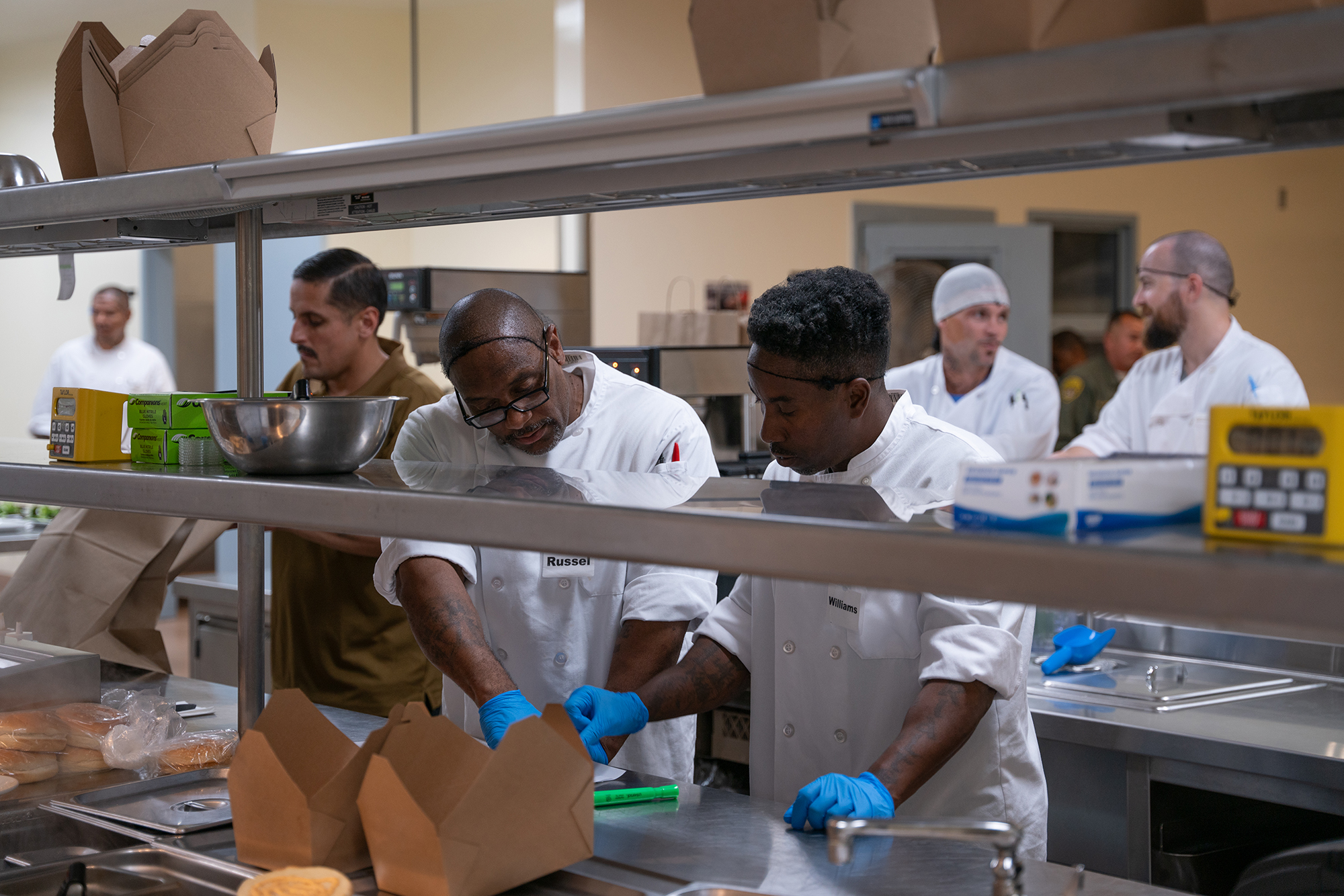 Inmates work in the Delancey Street Restaurant kitchen at the California State Prison Solano in Vacaville on July 24, 2024. "We actually built this restaurant," said Ray Williams, Jr., front right. "We started with hard hats and elevated to smocks." Photo by Florence Middleton, CalMatters