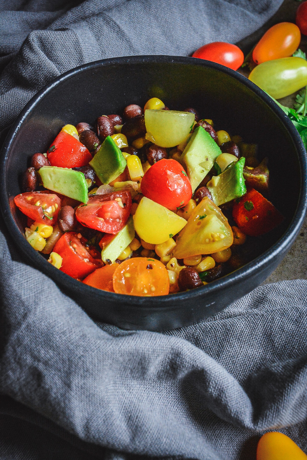 Mexican Tomato Salad with Black Beans, Corn, and Avocado in black bowl with tomatoes