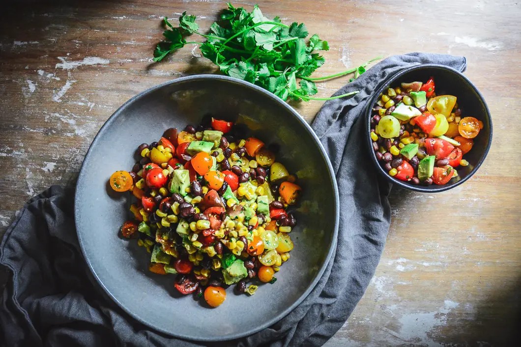Mexican Tomato Salad with Black Beans, Corn and Avocado in bowl with smaller bowl next to it and grey napkin.