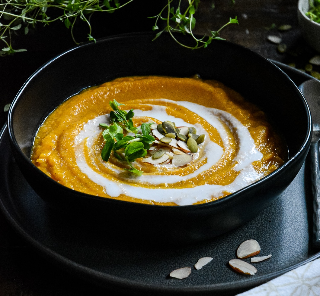 Butternut squash soup in black bowl with coconut cream and pumpkin seeds.