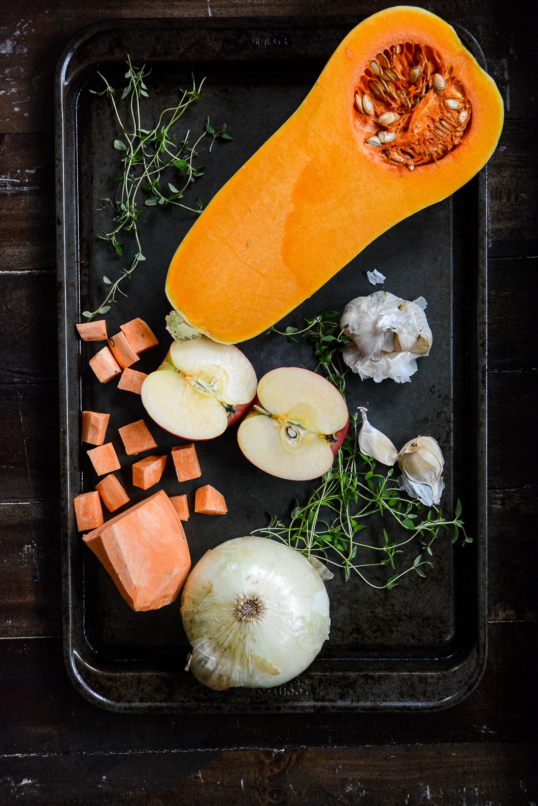 Roasting tray with half of butternut squash, cut up sweet potato, garlic, onion, apple and greens