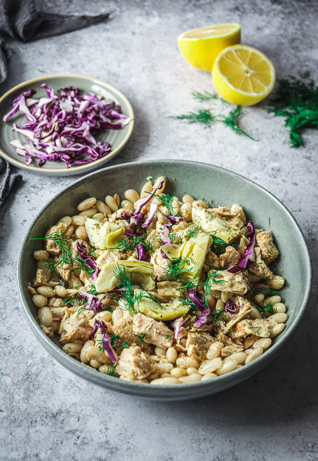White Bean Tuna Salad with Artichoke Hearts in bowl, sliced cabbage and lemon halves