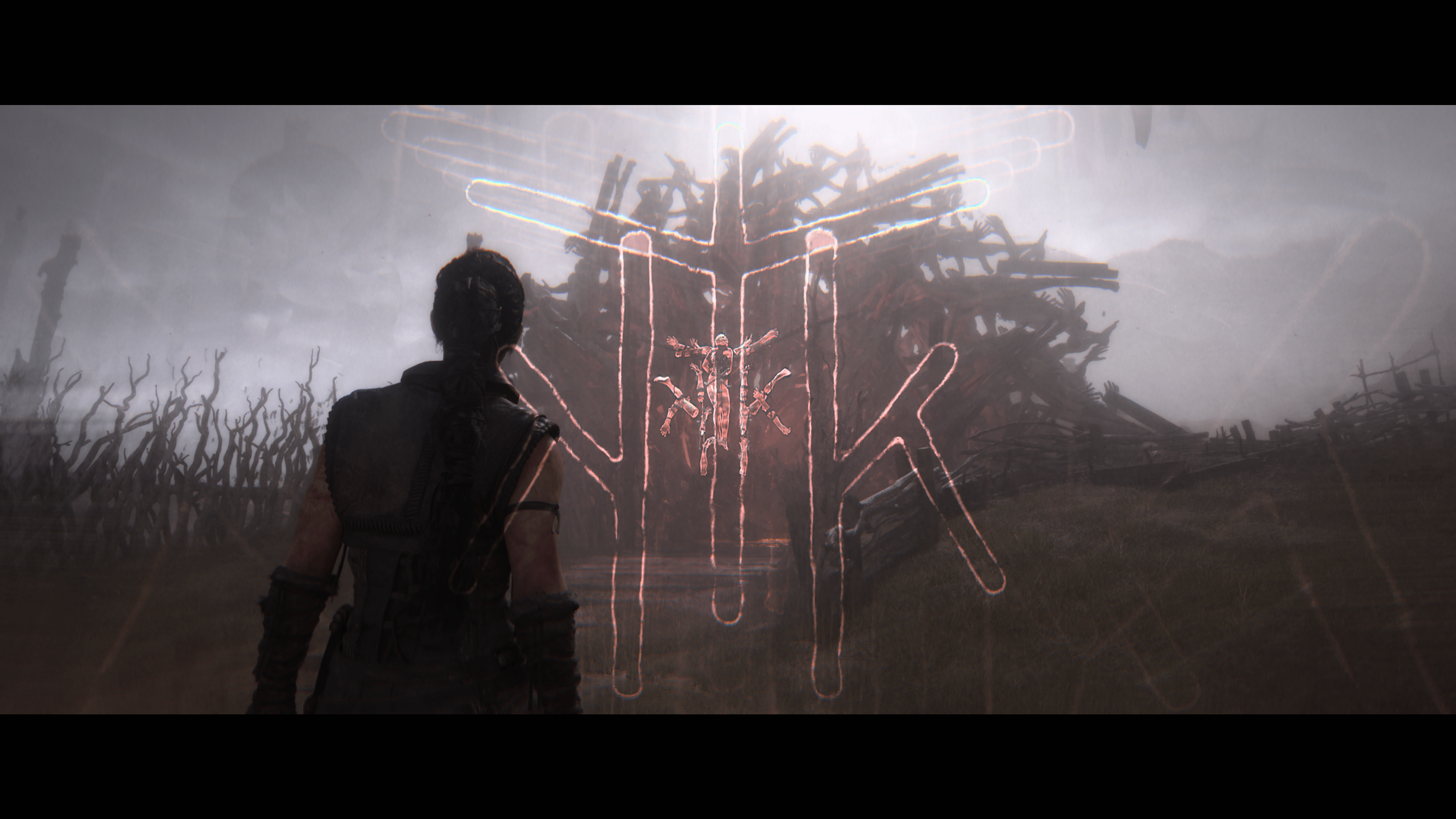 Looking from behind Senua towards a glowing symbol on an obstacle. A large outline of the same symbol is shown in the foreground.