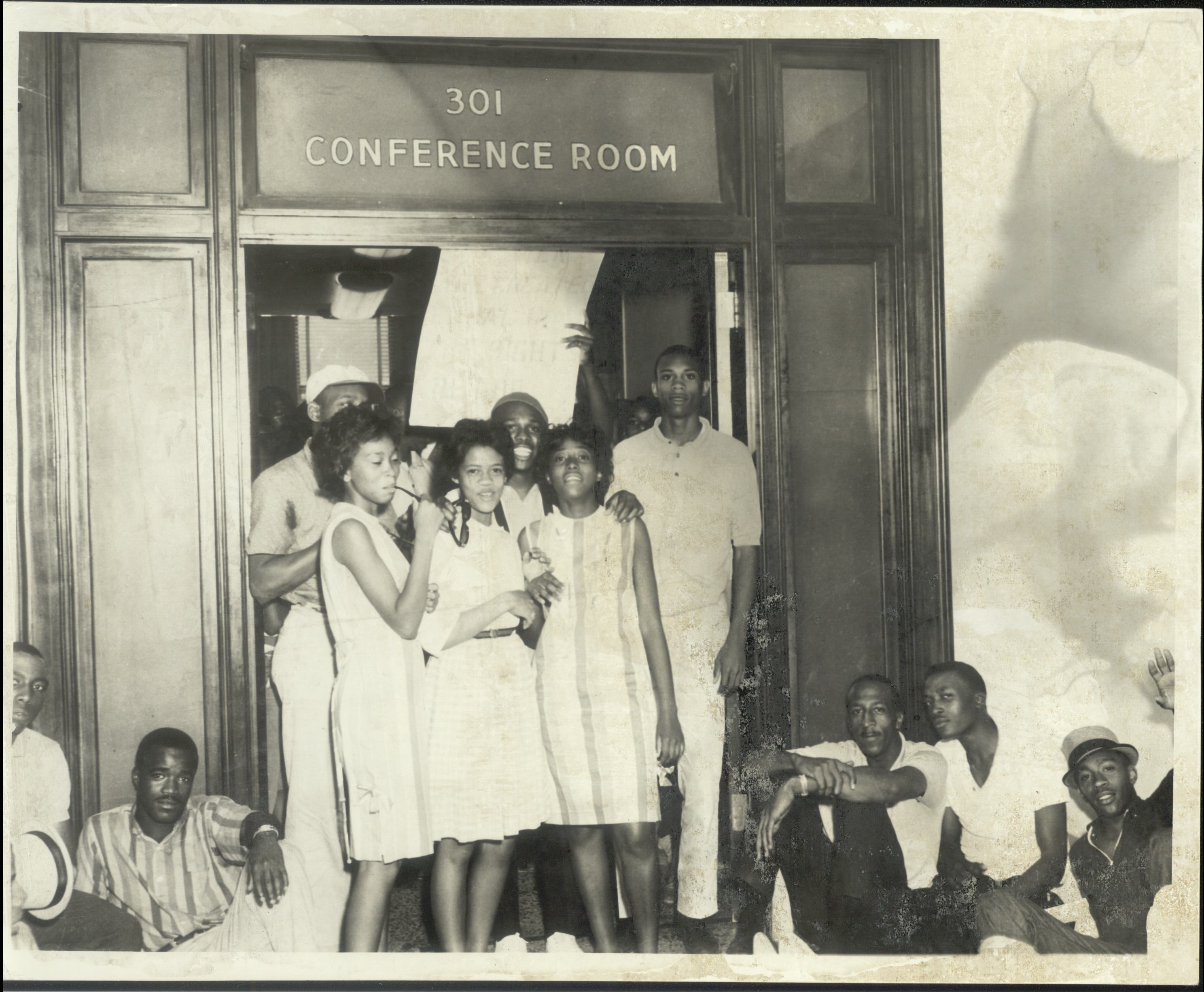 Several men and women stand in the doorway of a conference room in the Danville municipal building while other demonstrators sit on the floor in front of them