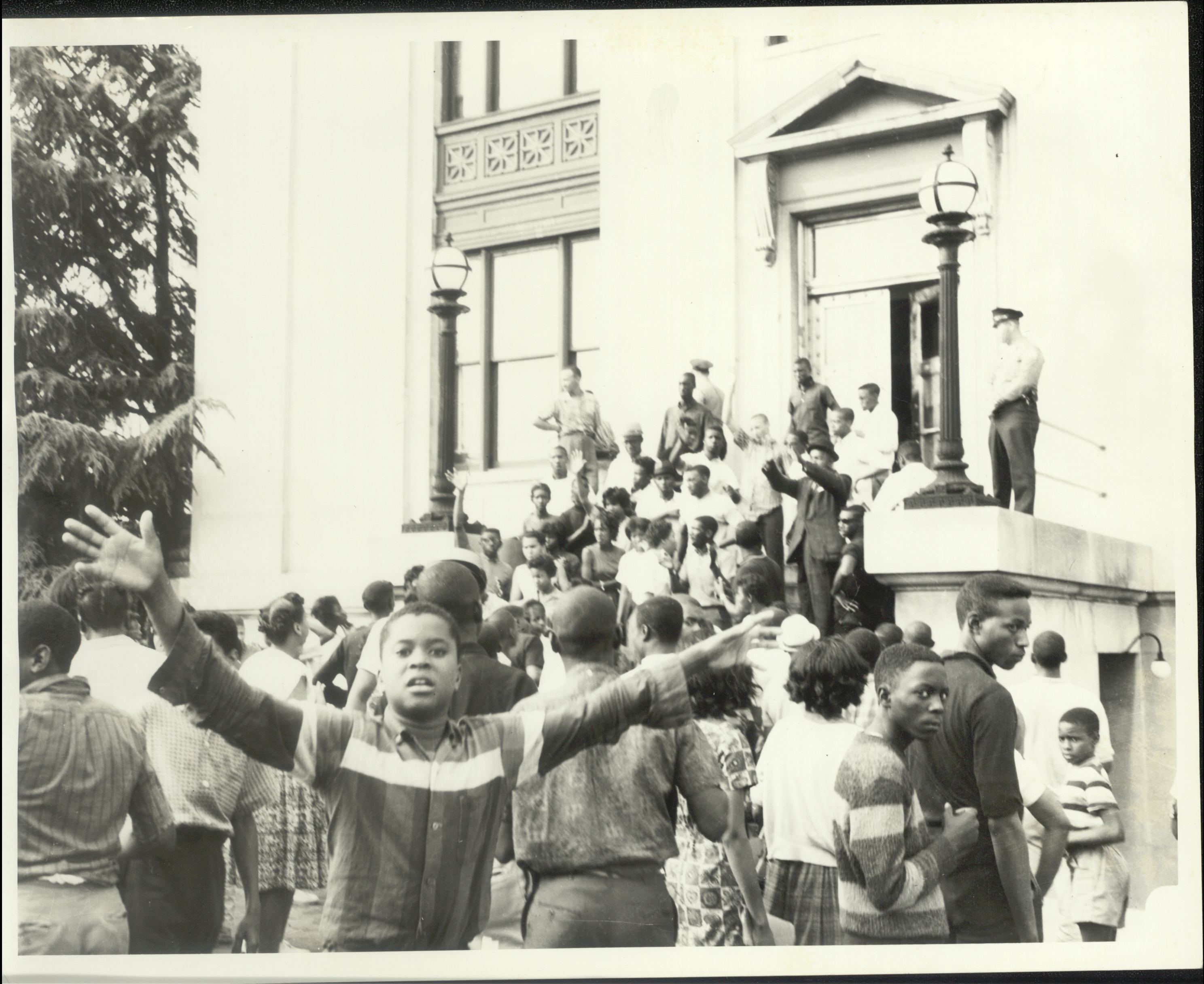 A large group of demonstrators, including both adults and children, stands on the steps in front of the Danville municipal building