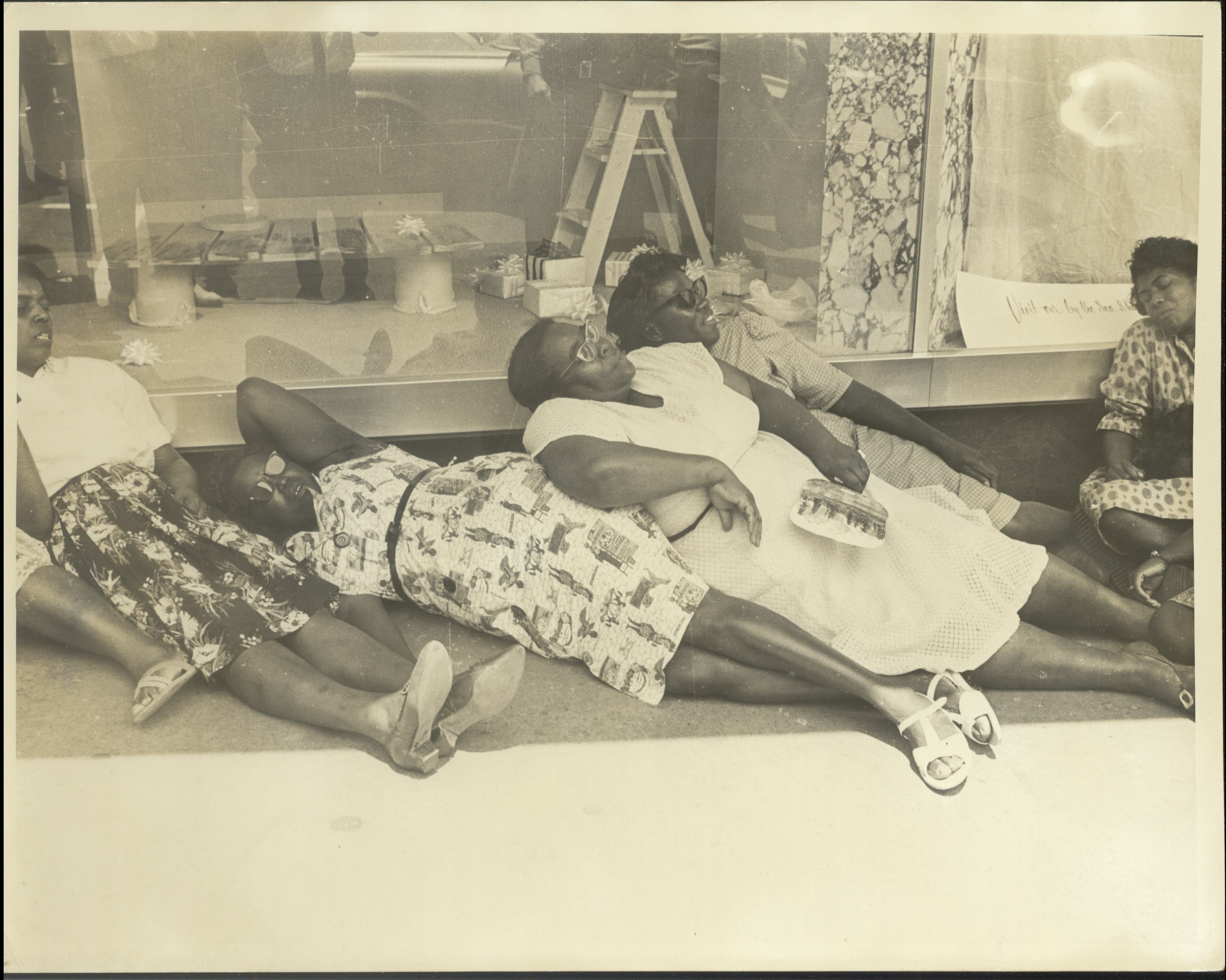 Several women lie on the ground in front of a Danville department store window