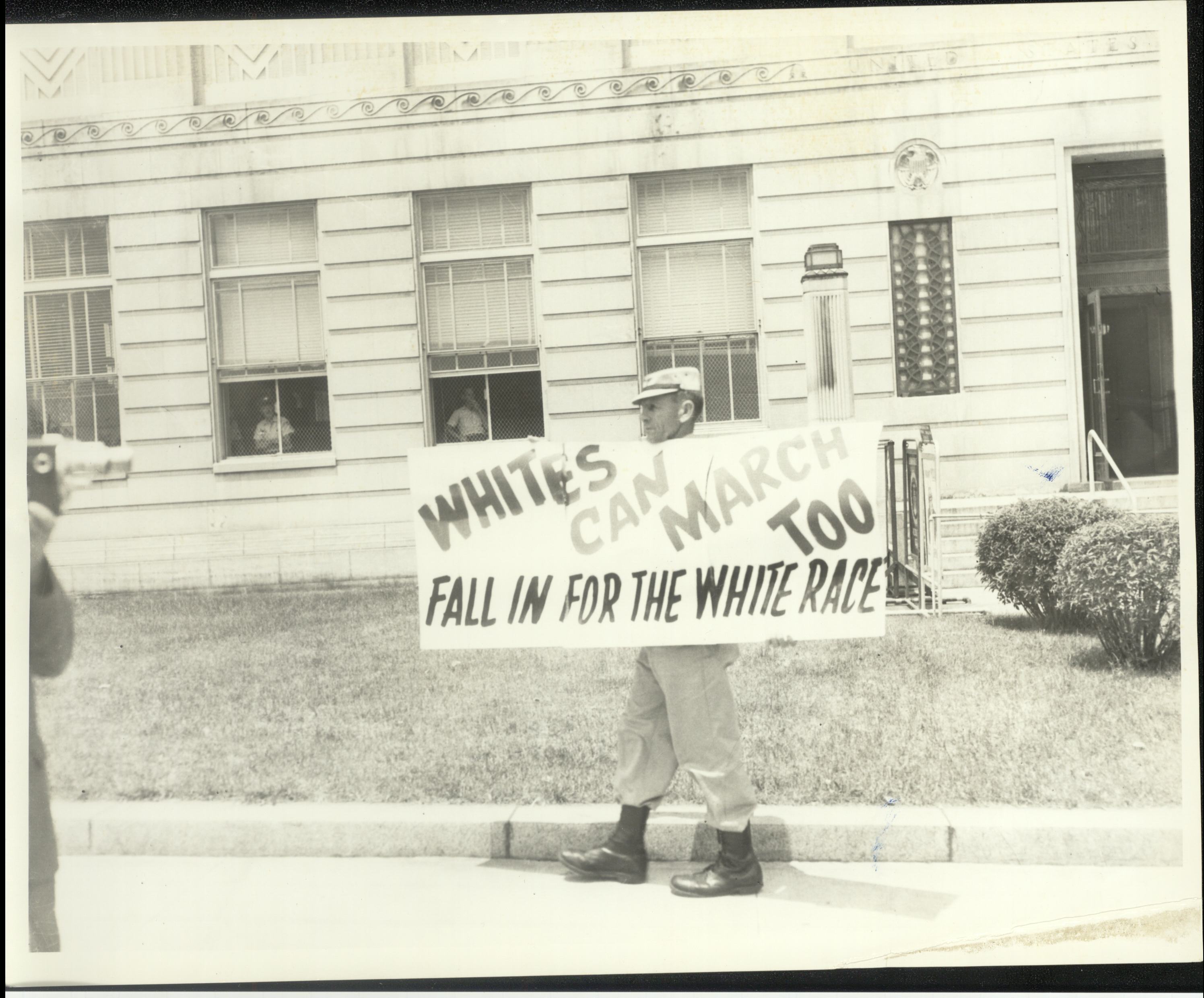 A man stands in front of the Danville post office holding a sign that says "Whites can march too. Fall in for the white race"