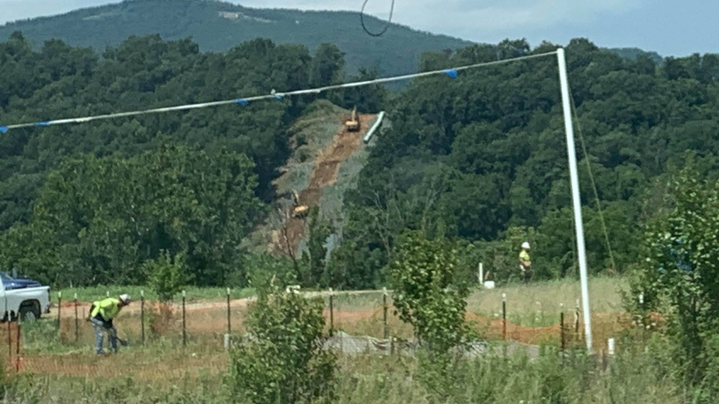 A pipeline path cleared up the side of a green mountain, with a pasture in the foreground.
