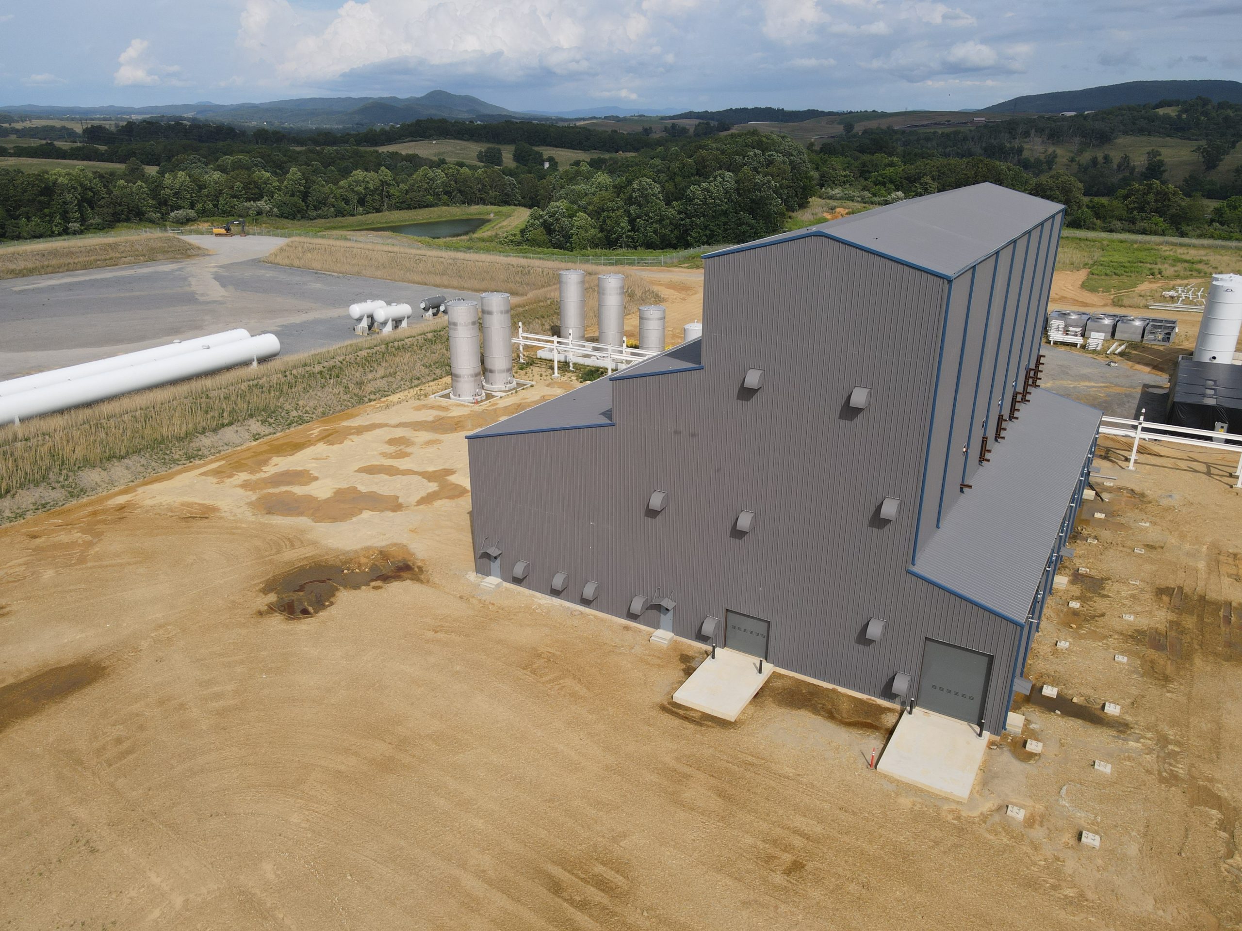 Photo of large gray industrial building on a dirt lot.