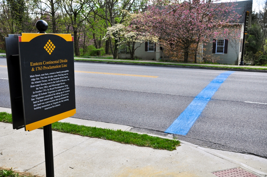 The town of Blacksburg marks the Proclamation Line of 1763 and the Eastern Continental Divide with this sign at the corner of Sunset Boulevard and South Main Street and blue line painted across South Main. Town of Blacksburg photo.