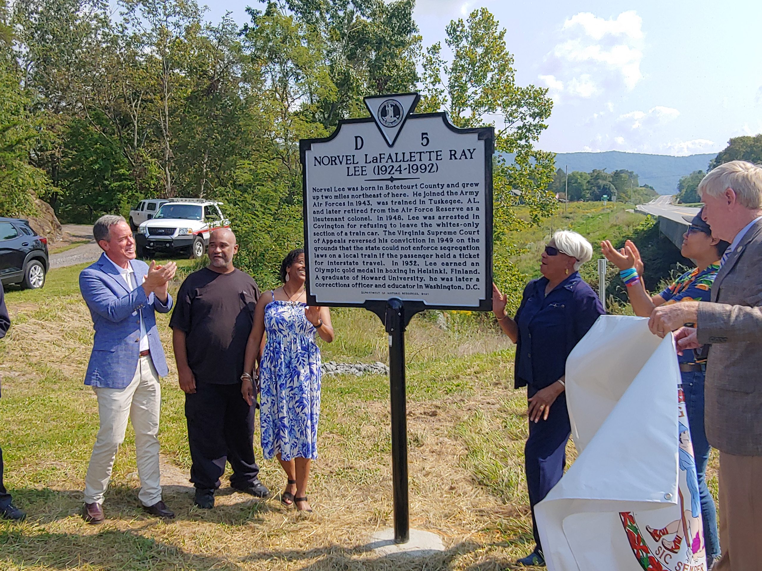 A group of family and friends stands around a state historical marker telling the story of Norvel Lee of Botetourt County, the first Black Olympic gold medalist and a civil rights pioneer.