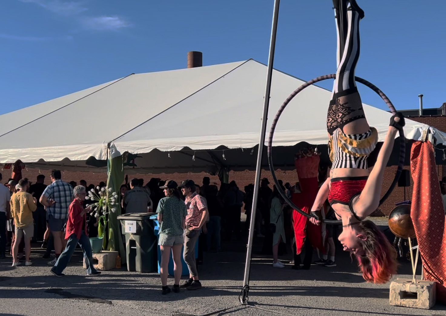 An aerial dancer performs hanging upside down outside a tent.