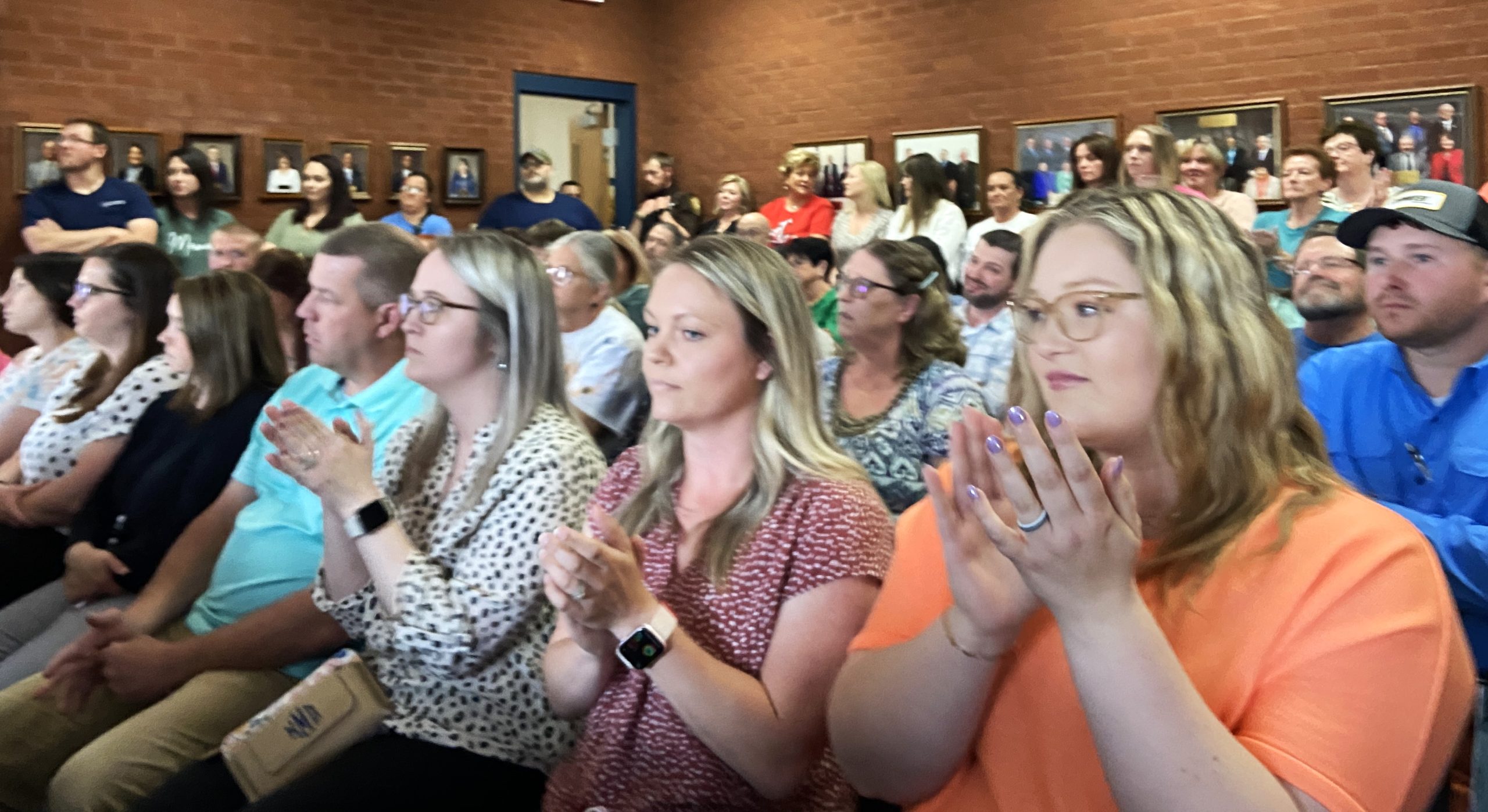 A crowd of people fills chairs and stands against the walls at a public hearing before the Russell County School Board.