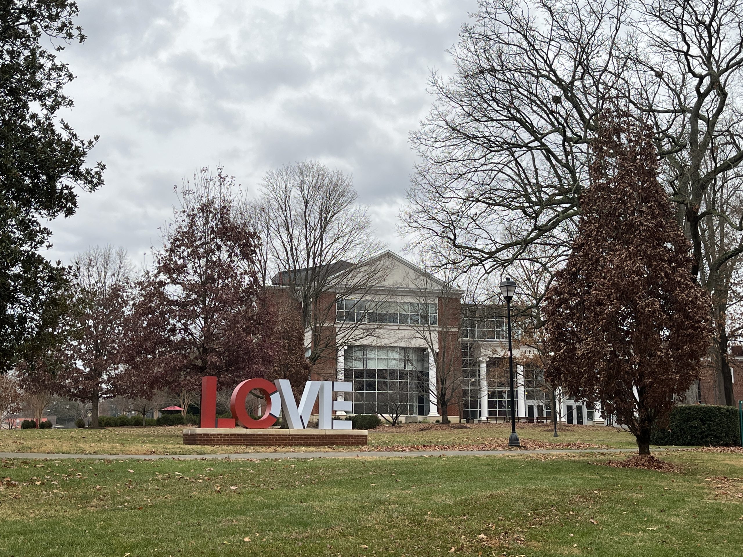 An exterior photo of a red brick building at the back of a green lawn, with a red and white "LOVE" sculpture in the middle ground.